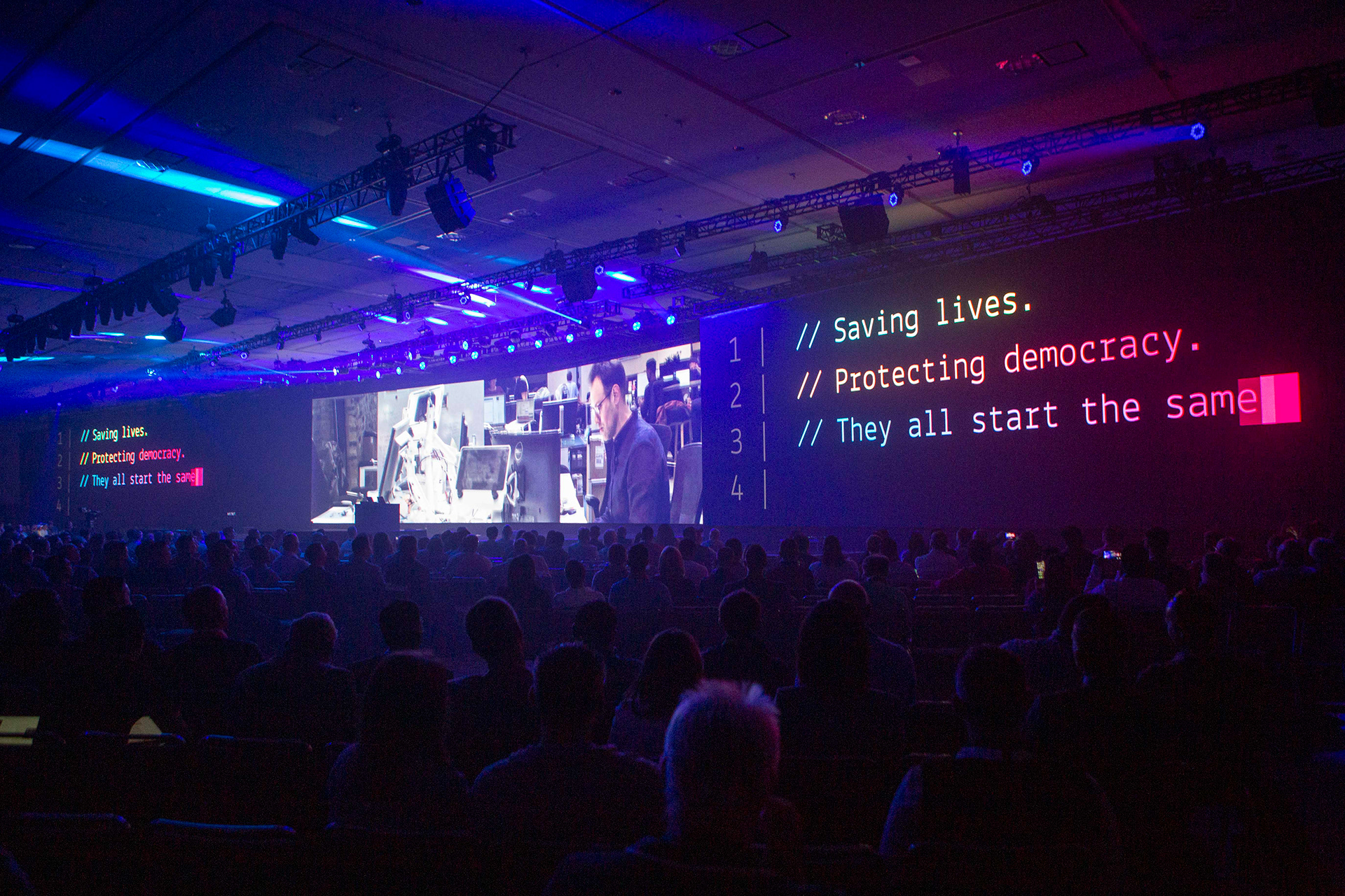 Keynote slide reading Saving lives. Protecting democracy. on wide screen with audience silhouettes